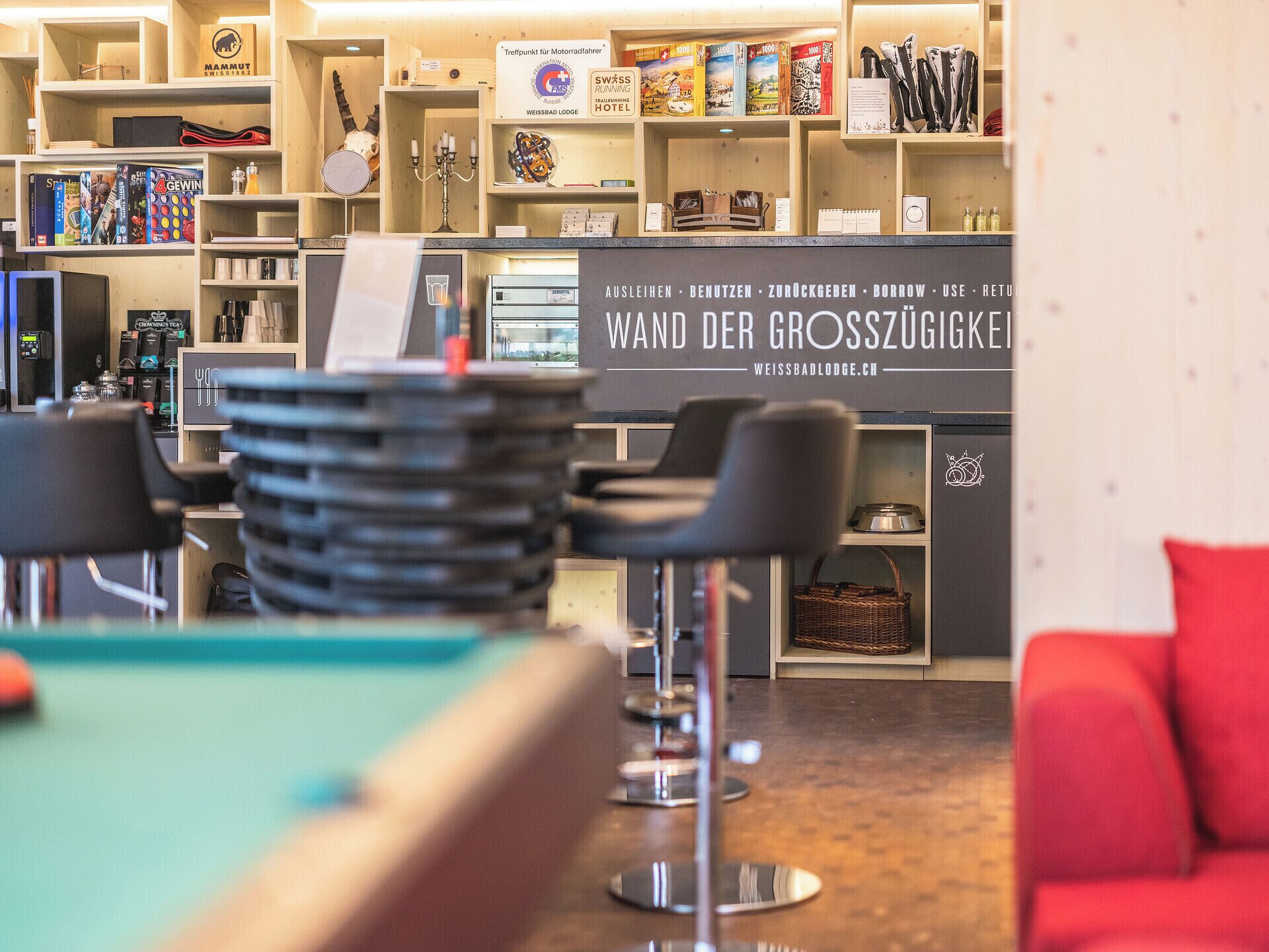 A hotel lobby with a pool table, bar area, and various amenities including books and a sign for the Swiss Running Hotel.