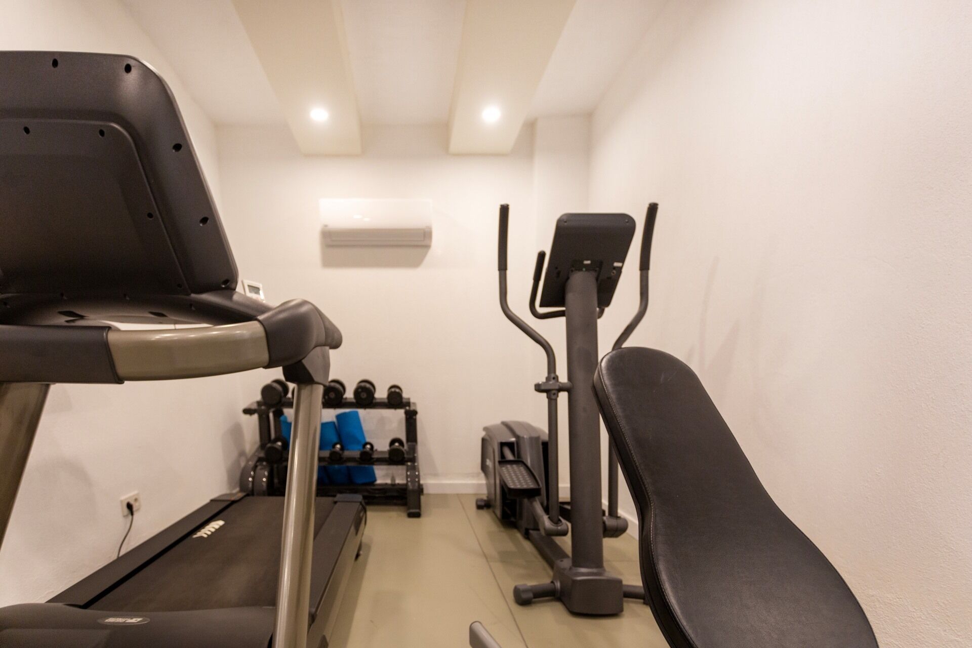 Ein Fitnessstudio mit Laufband, Crosstrainer und Krafttrainingsgeräten.