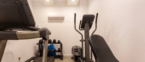 Ein Fitnessstudio mit Laufband, Crosstrainer und Krafttrainingsgeräten.