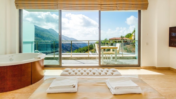 Une chambre moderne dotée d’une grande fenêtre, d’une baignoire, d’un canapé et d’un coin repas offrant une vue sur les montagnes.