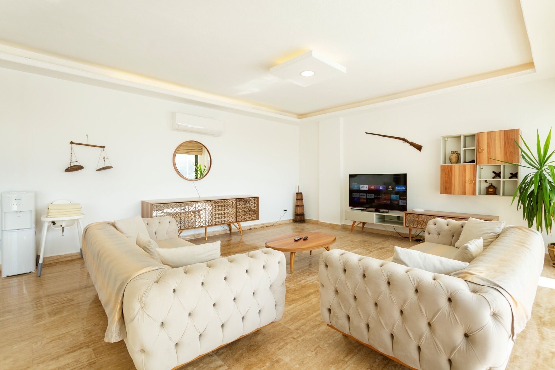 A modern living room with a sectional sofa, a coffee table, a TV, and a decorative wall with a balance scale and mirror.