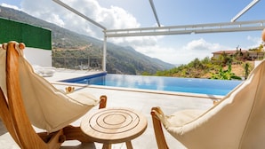 Un espace aménagé au bord de la piscine, avec deux hamacs et une petite table, offrant une vue sur un paysage montagneux.