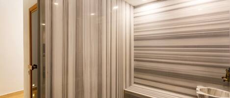 A modern bathroom with a marble wall, a sink, and a shower area.