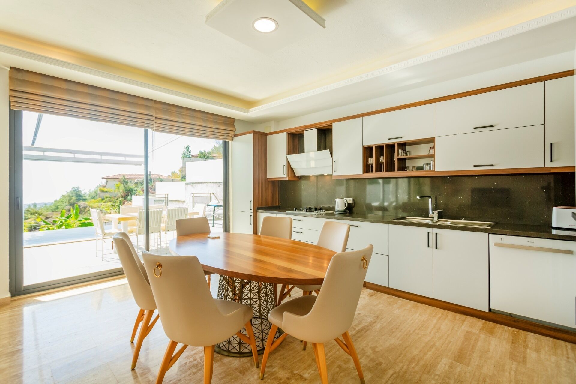 Een moderne keuken met een eethoek, met een grote tafel en stoelen, witte kasten en uitzicht door de glazen deur.