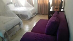 A room with two beds covered in white sheets, a purple sofa, and a wooden table with a computer. - Golden Moon Star (Nairobi)