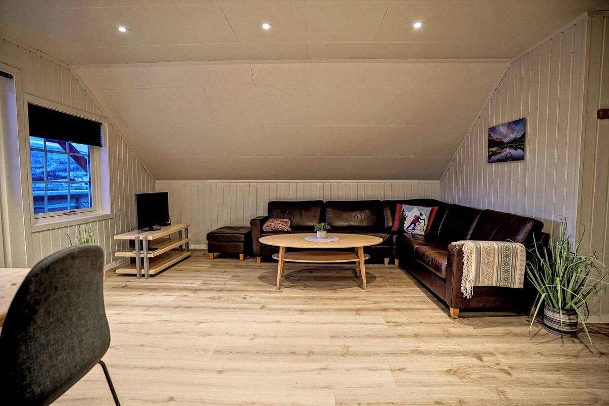 A cozy living room with a wooden floor, a brown leather sofa, a coffee table, and a TV on a stand.