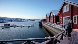 Un bâtiment en bois rouge avec une jetée qui s’avance dans une étendue d’eau, le tout étant entouré de neige.