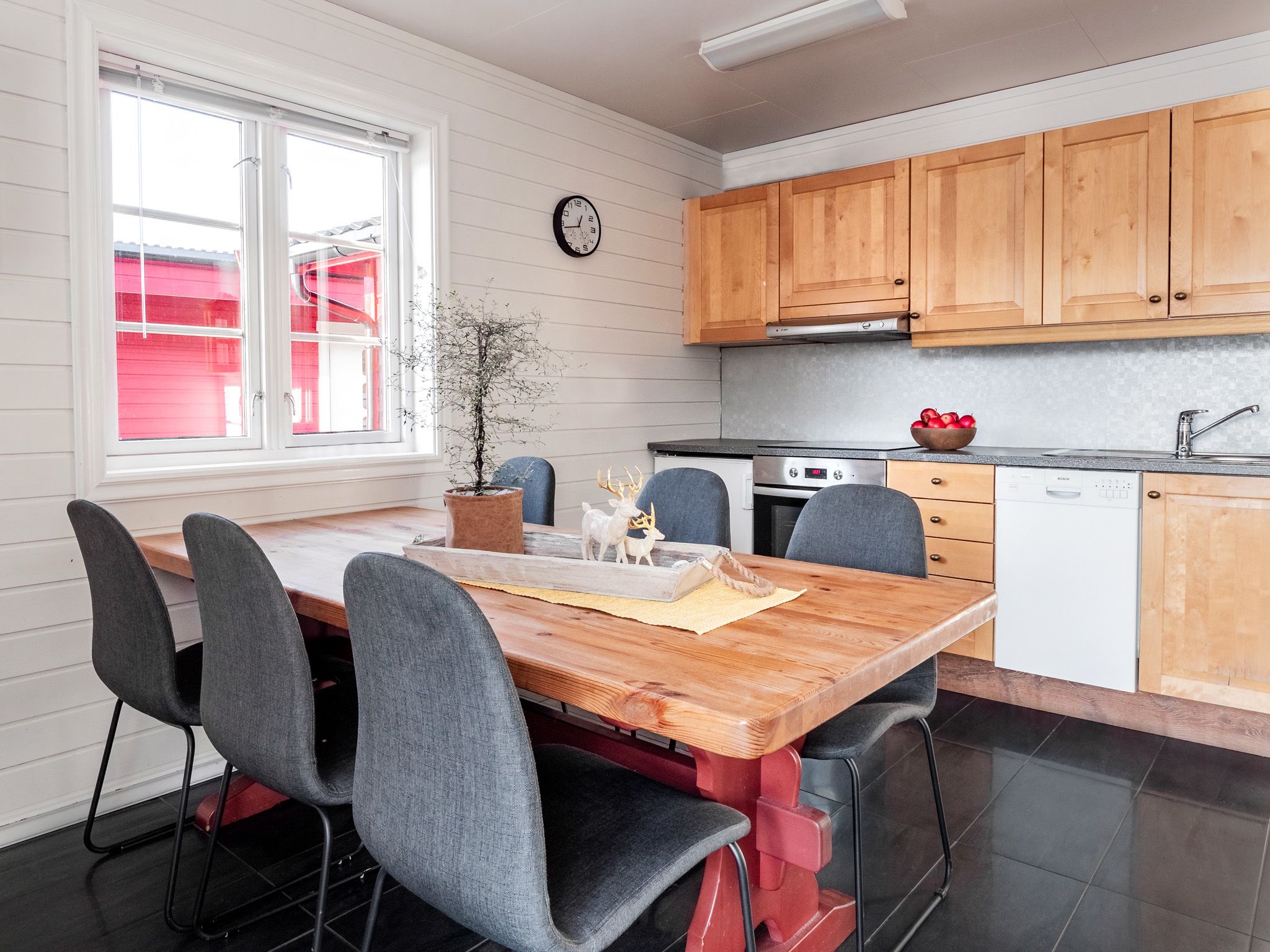 Una cocina moderna con armarios de madera, un lavavajillas Bosch y un comedor con mesa de madera y sillas grises.