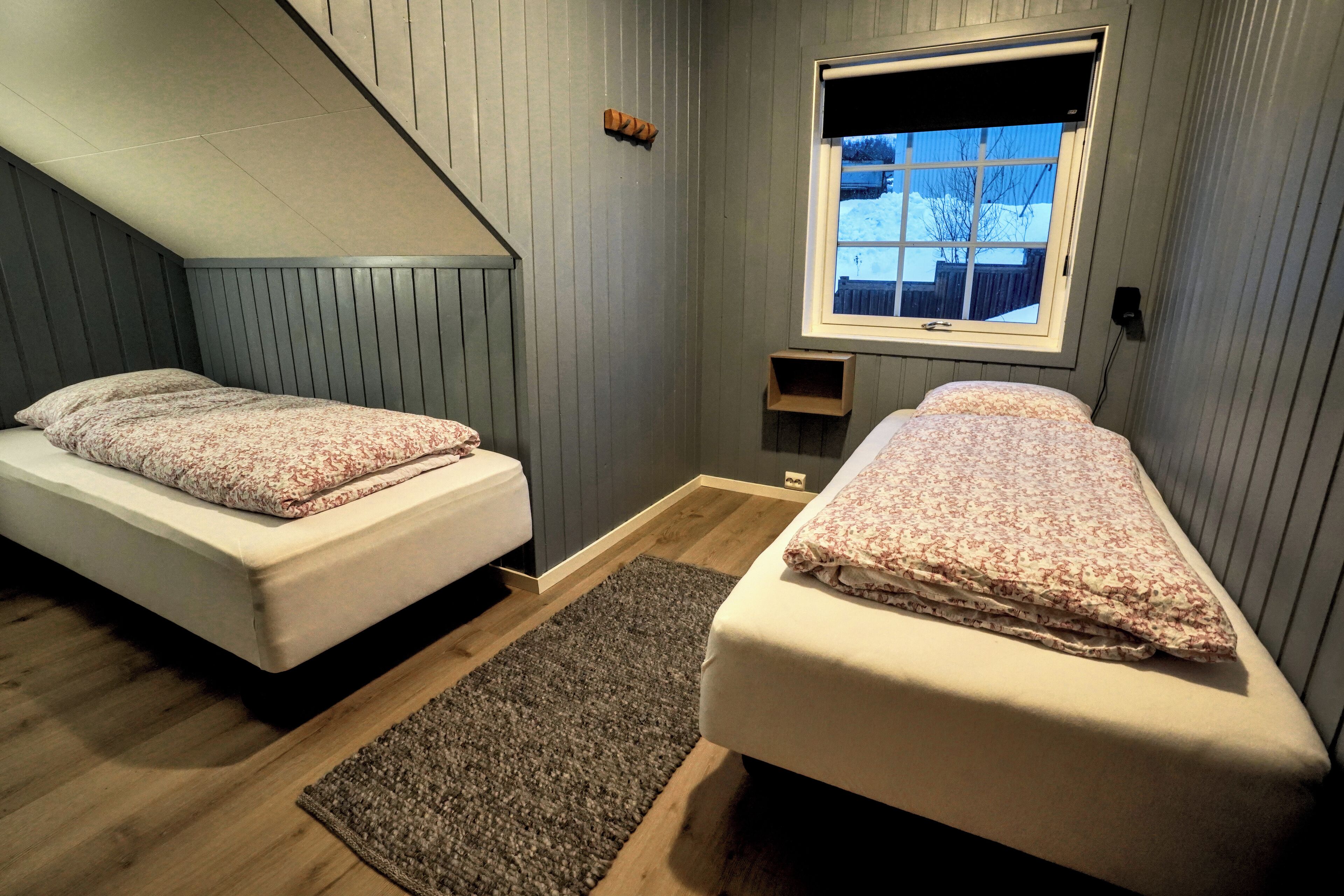 A bedroom with two single beds, a window with a view of a snowy landscape, and a sloped ceiling.