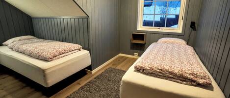 A bedroom with two single beds, a window with a view of a snowy landscape, and a sloped ceiling.