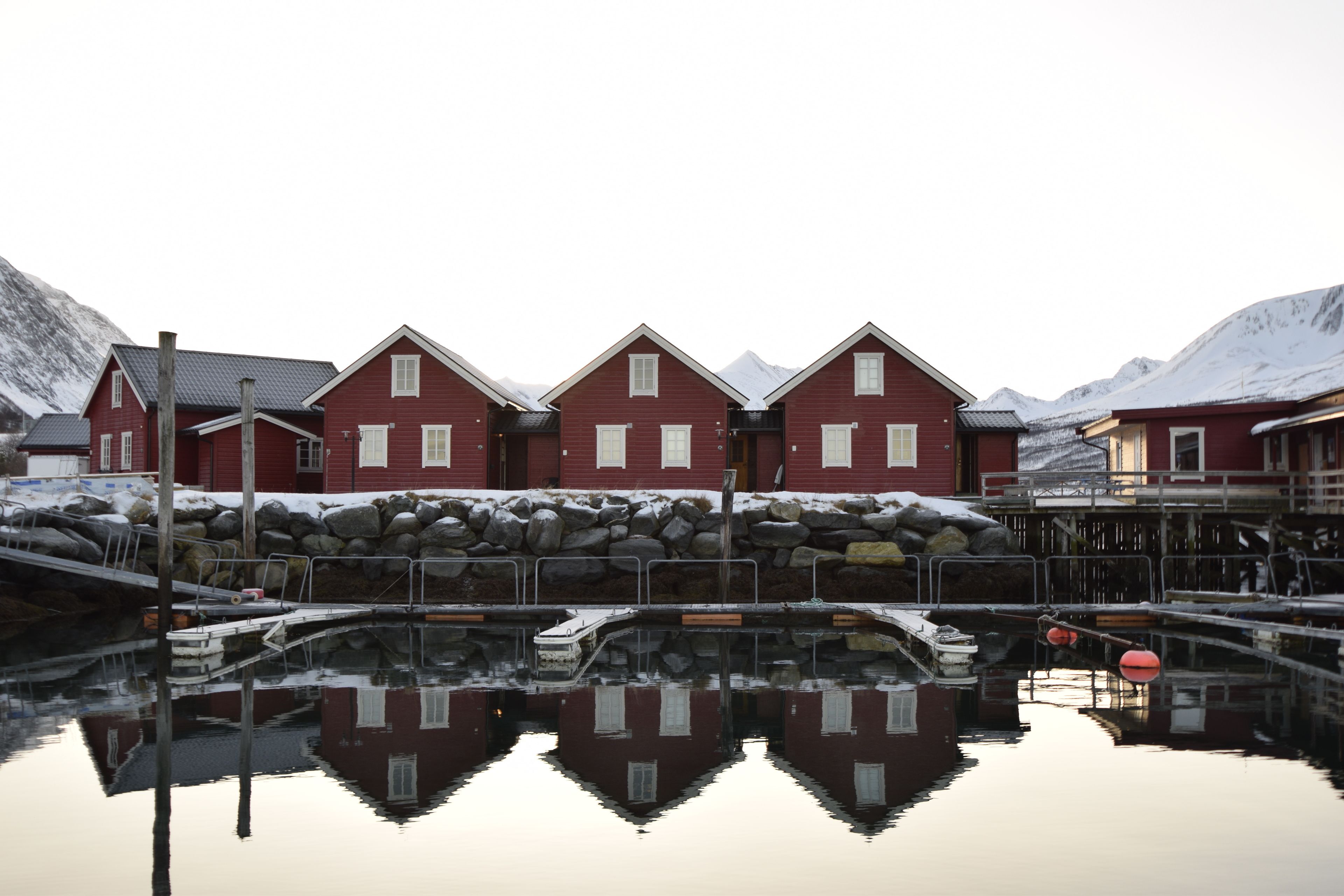 Une rangée de bâtiments rouges, avec un quai et des eaux calmes qui les reflètent.