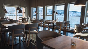 Un restaurant avec des tables et des chaises, de grandes fenêtres et des lampes suspendues.