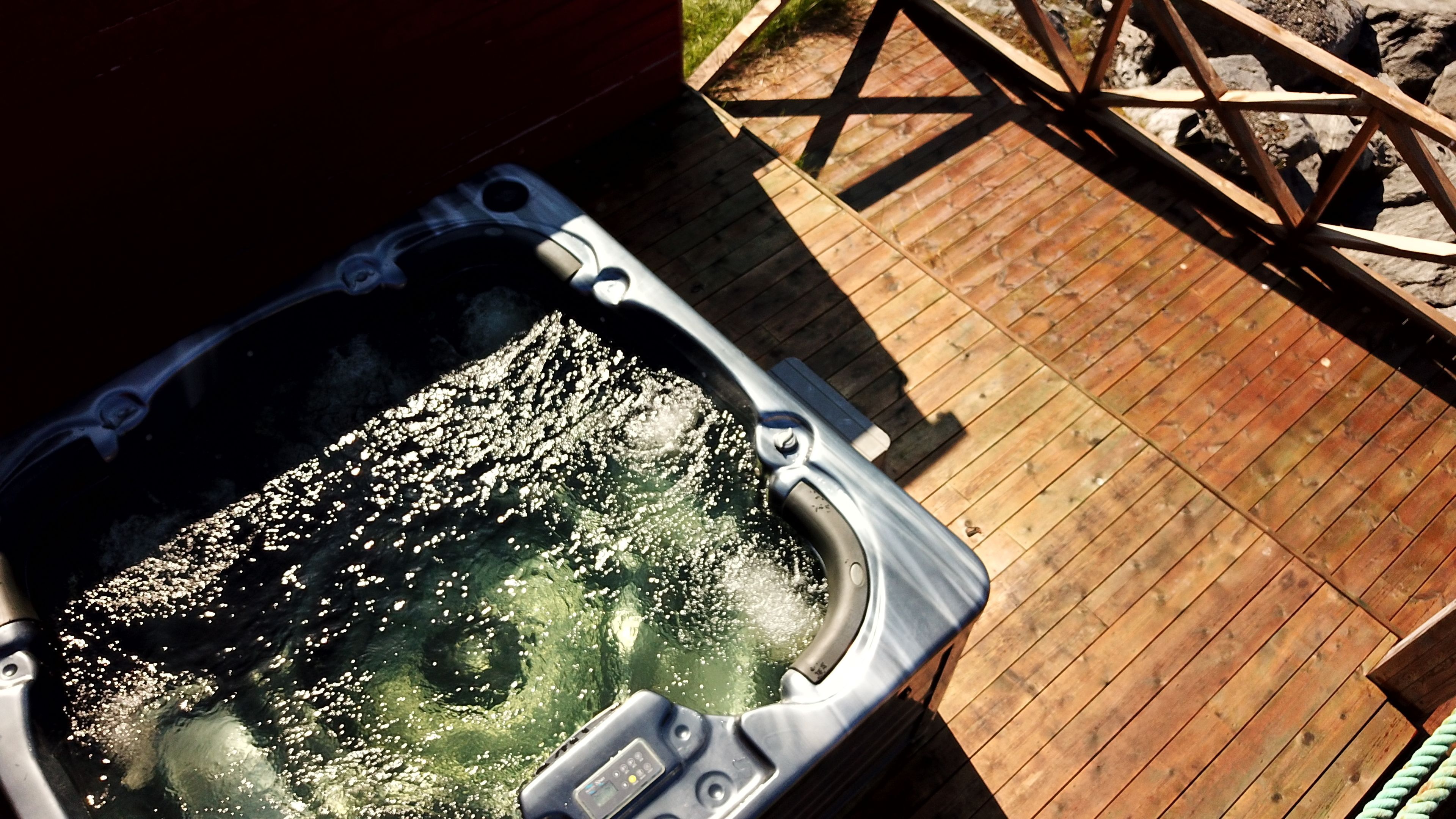 Un jacuzzi en una terraza de madera con barandilla de metal.