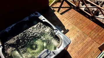 Un jacuzzi en una terraza de madera con barandilla de metal.