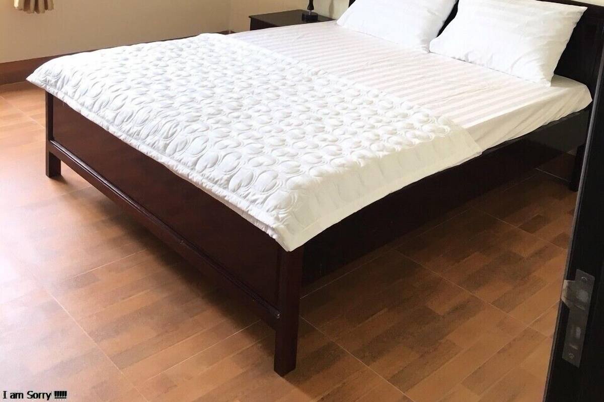 A bedroom with a large bed, a nightstand, a lamp, and an air conditioning unit on the wall.