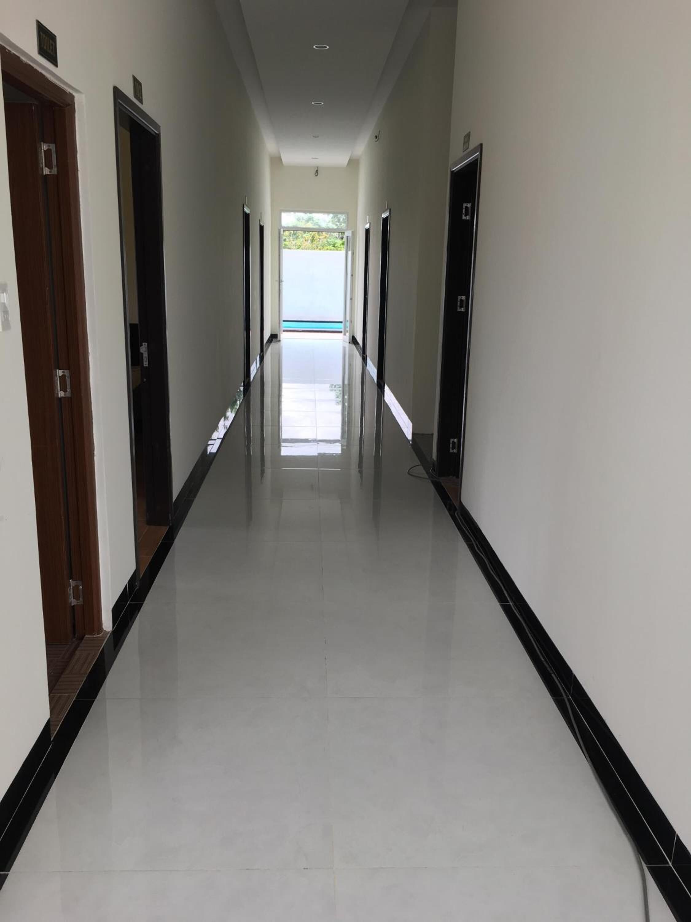 Um corredor comprido e estreito, com paredes brancas e detalhes em preto, que leva a uma saída iluminada.