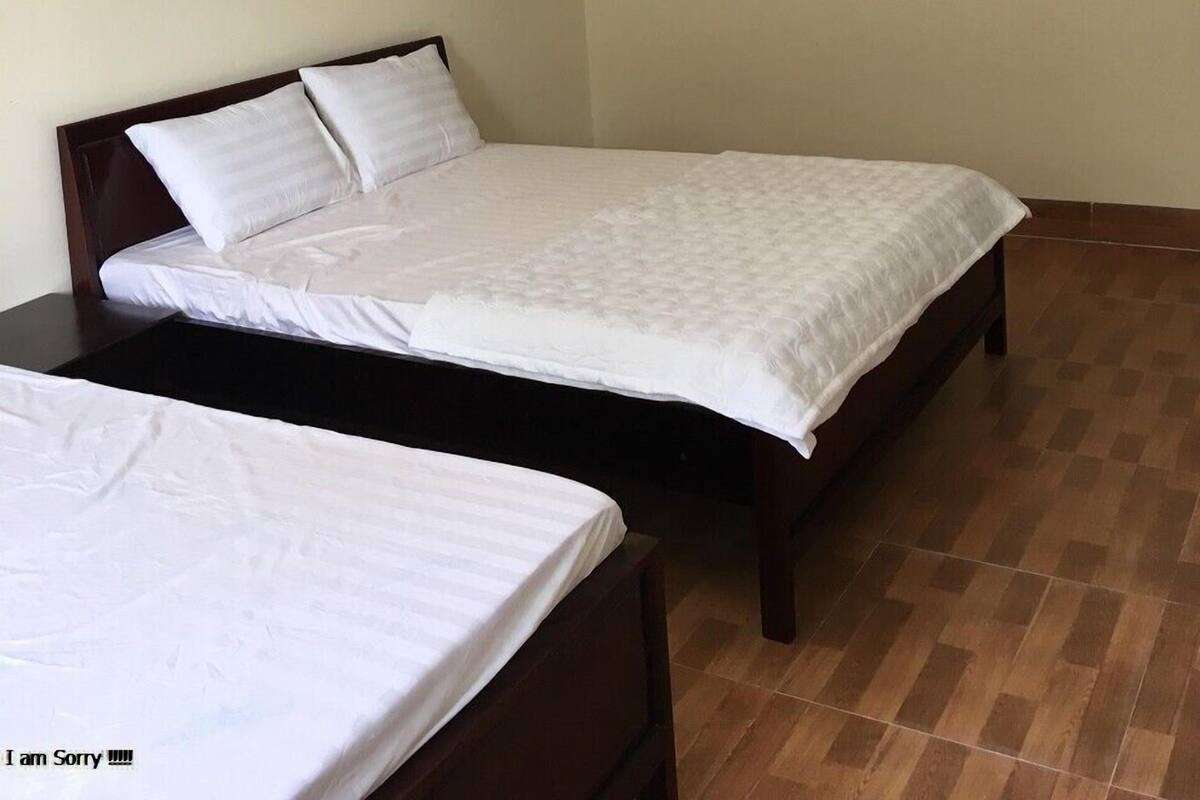 A small, clean room with two single beds, a wall-mounted air conditioner, and a tiled floor.