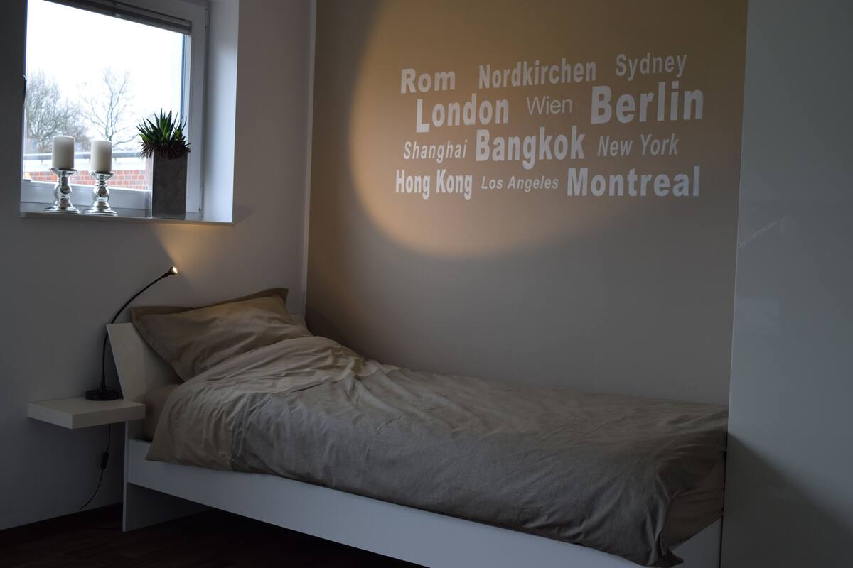 A minimalist bedroom with a bed, bedside table, and a wall with city names.