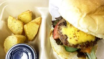 Una comida que incluye una hamburguesa con queso y lechuga, acompañada de unos trozos de patata sazonados.