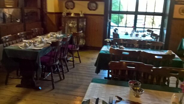 A dining area with wooden tables and chairs, a large window with a view of trees, and a clock on the wall. - Rhymney House hotel (Tredegar)