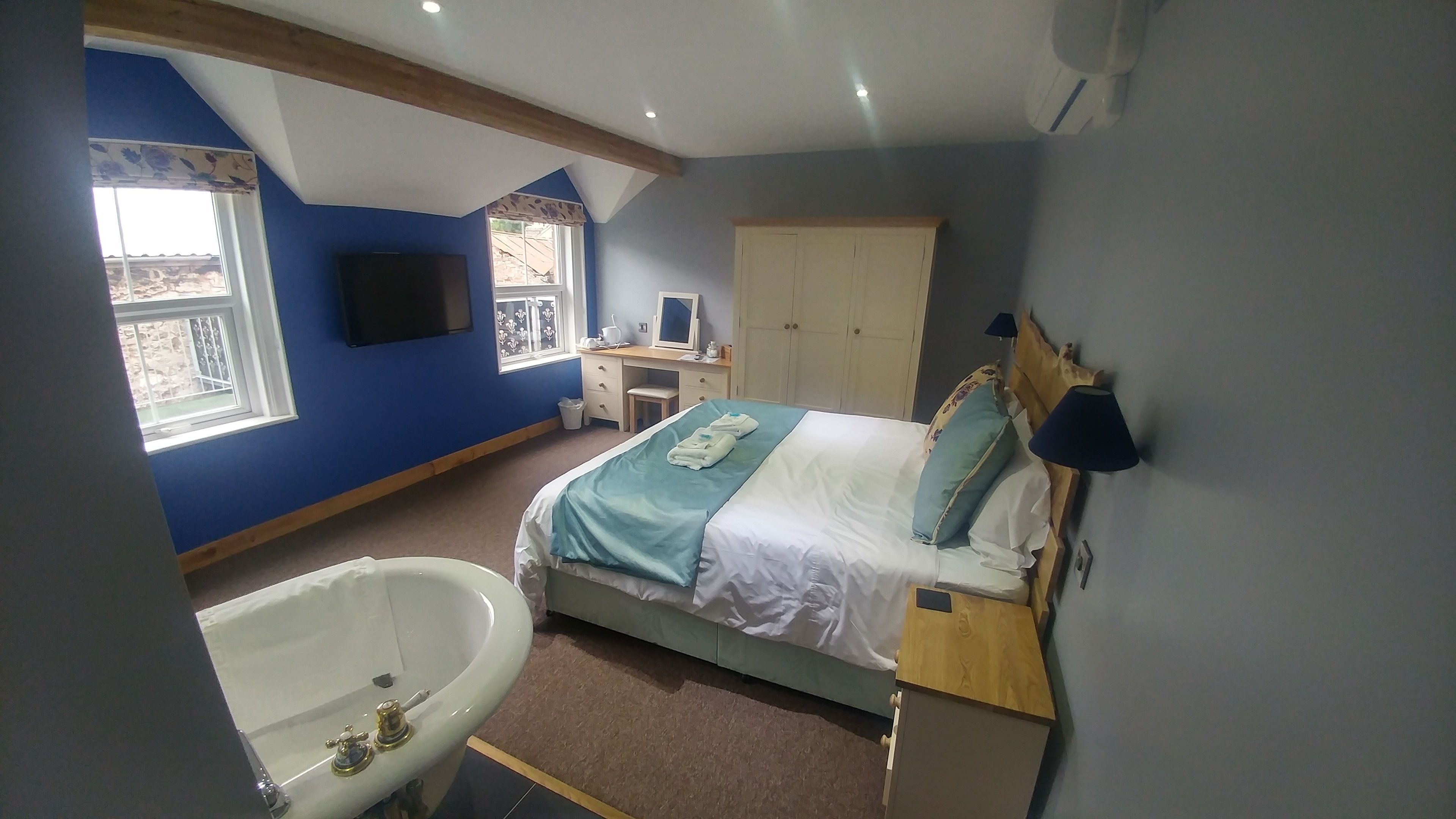 A bedroom with a bed, a desk, a wardrobe, and a bathroom with a bathtub.