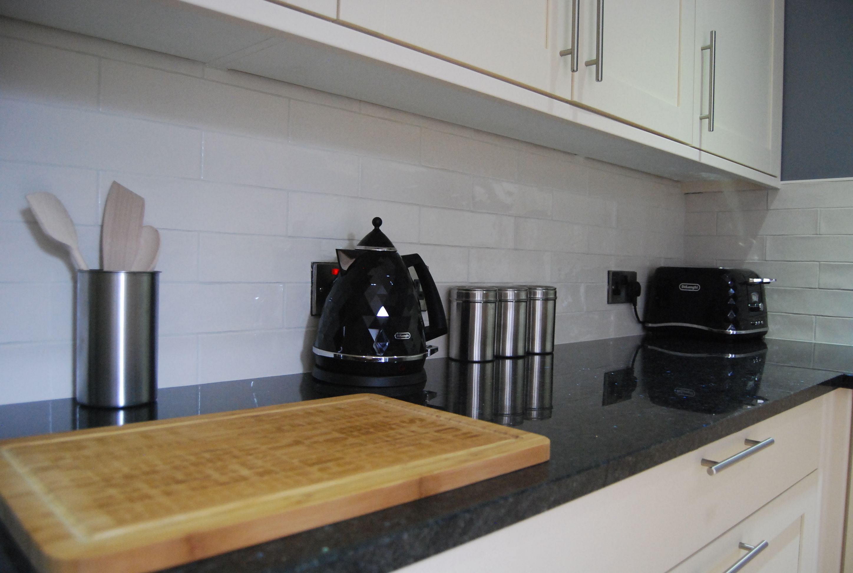 A kitchen with white cabinets, a black countertop, a wooden cutting board, a coffee maker, and stainless steel containers.