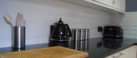 A kitchen with white cabinets, a black countertop, a wooden cutting board, a coffee maker, and stainless steel containers.