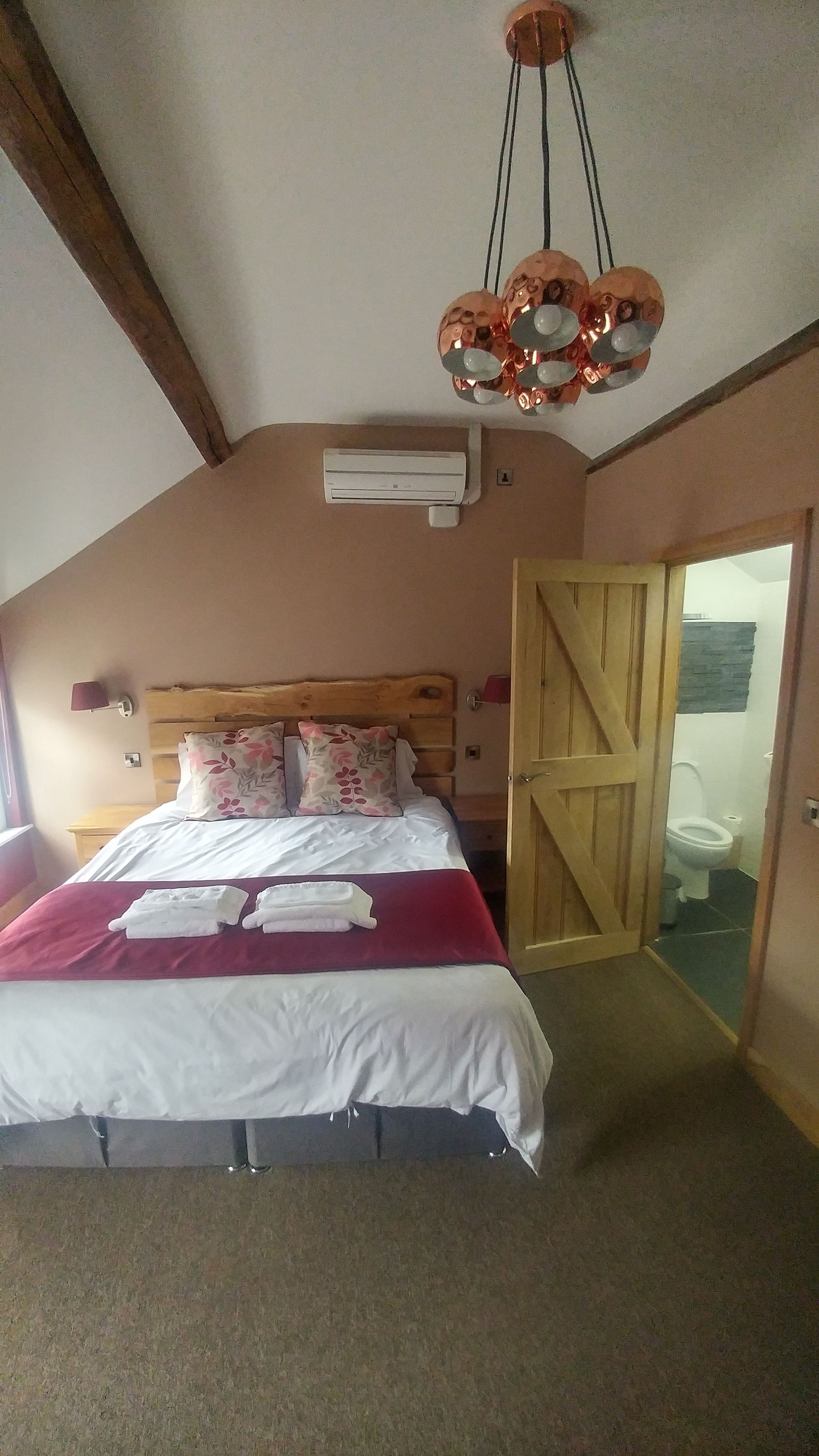 A bedroom with a wooden headboard, a bed with white and red bedding, a ceiling fan, and an air conditioning unit.