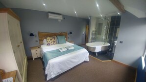 Un dormitorio con cama, mesitas de noche, un tocador, un ventanal grande y un baño con bañera y ducha.