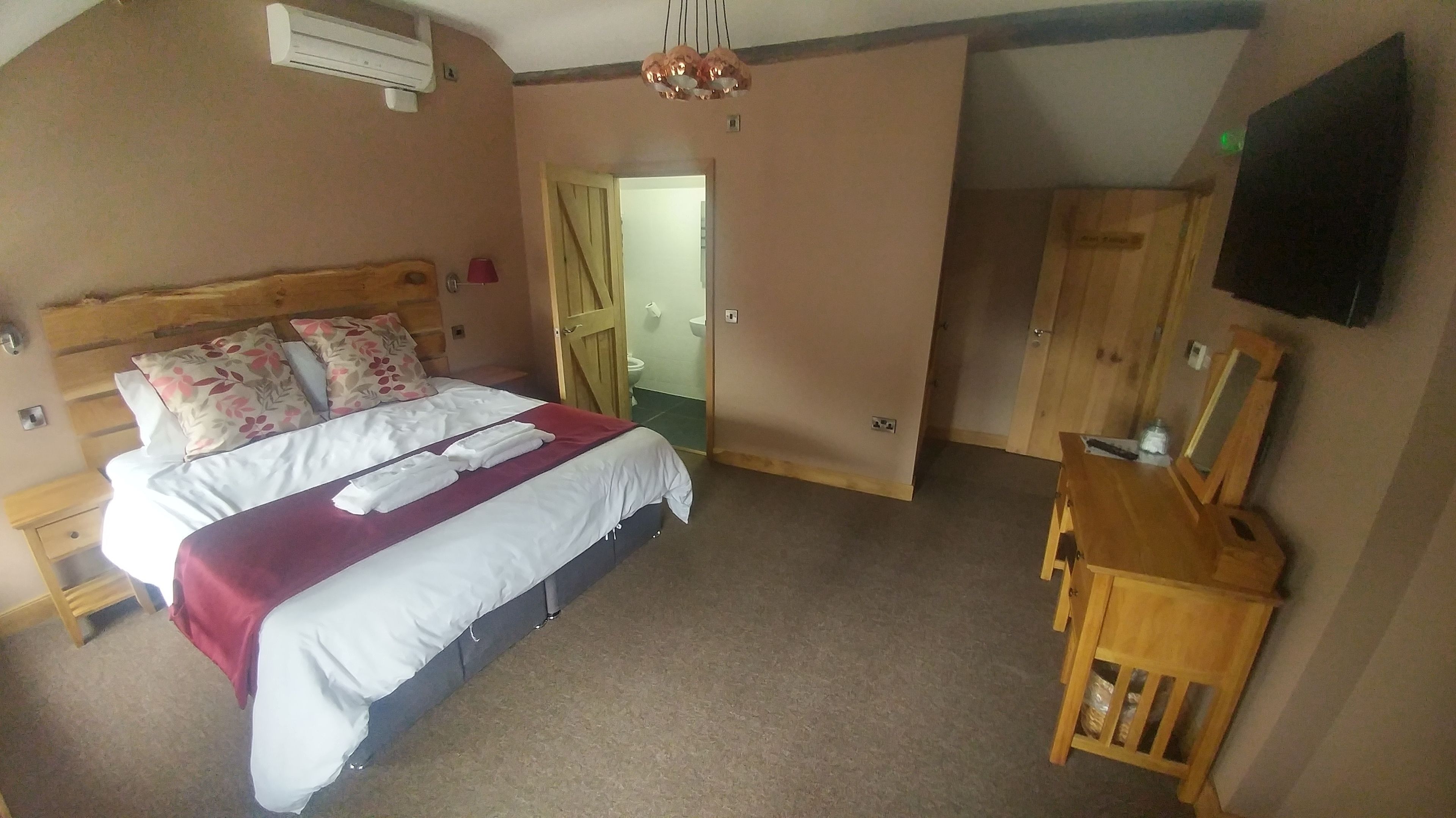 A bedroom with a bed, wooden headboard, a bedside table, a mirror, a wardrobe, and a television on the wall.