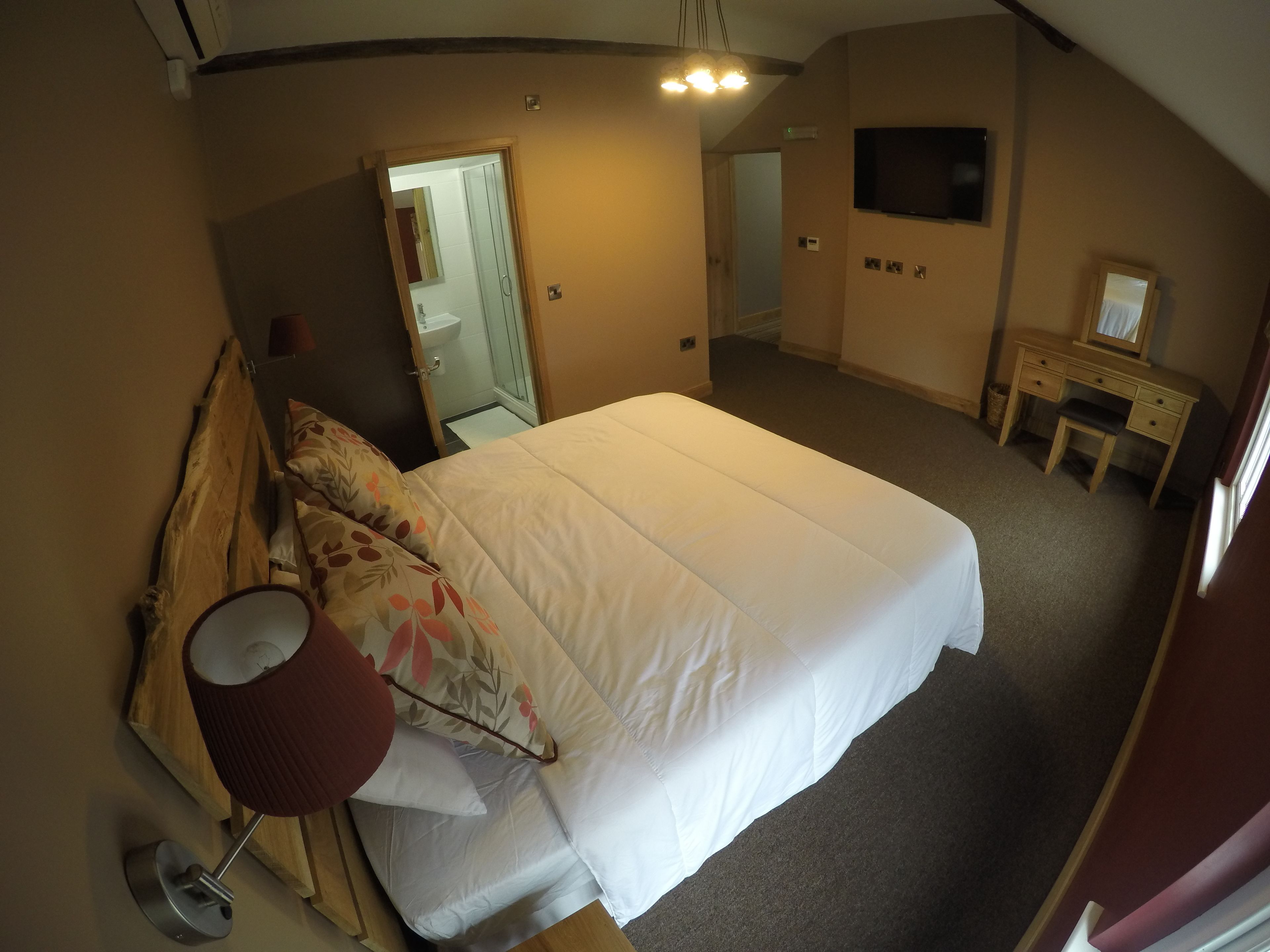 A bedroom with a bed, a desk, a mirror, and a TV.