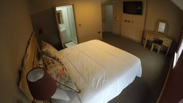 A bedroom with a bed, a desk, a mirror, and a TV.