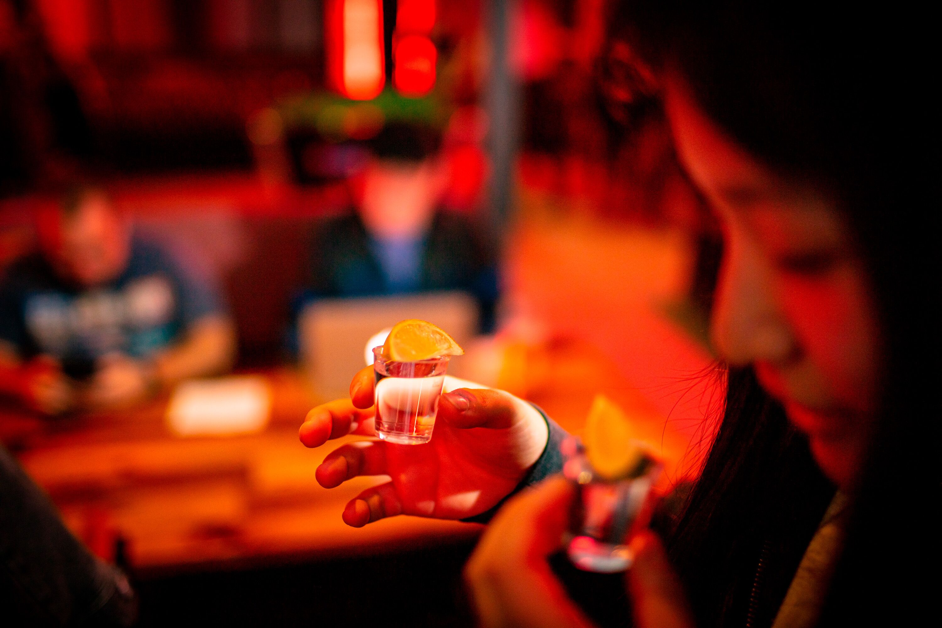 A person holding a shot glass with an orange slice.