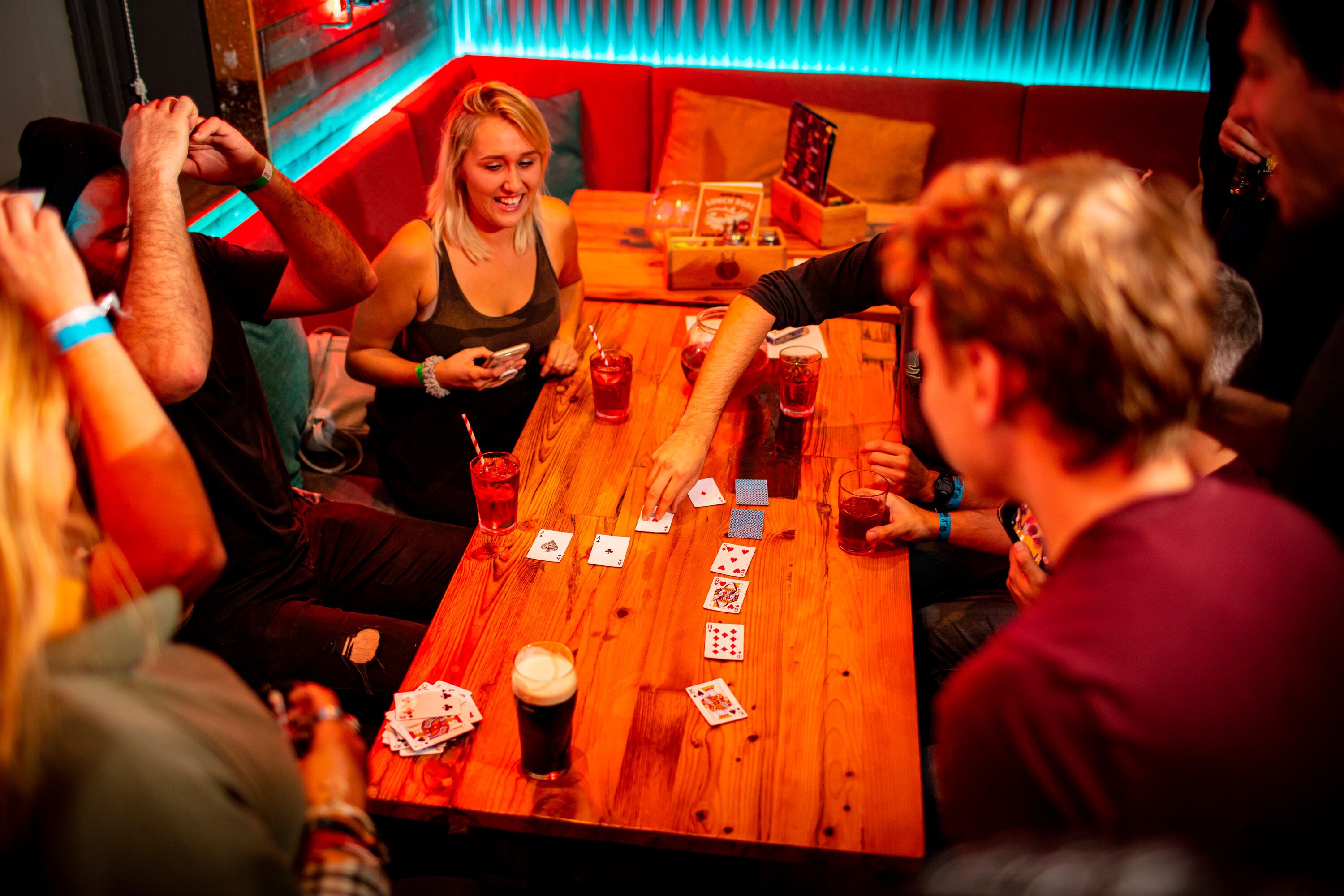 Un grupo de personas jugando cartas en una mesa de madera con bebidas.
