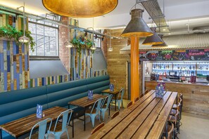 A restaurant with wooden tables and blue chairs, a blue booth seating area, and a brick wall with a mural. - Kick Ass Grassmarket - Adults Only - Hostel (Edinburgh)