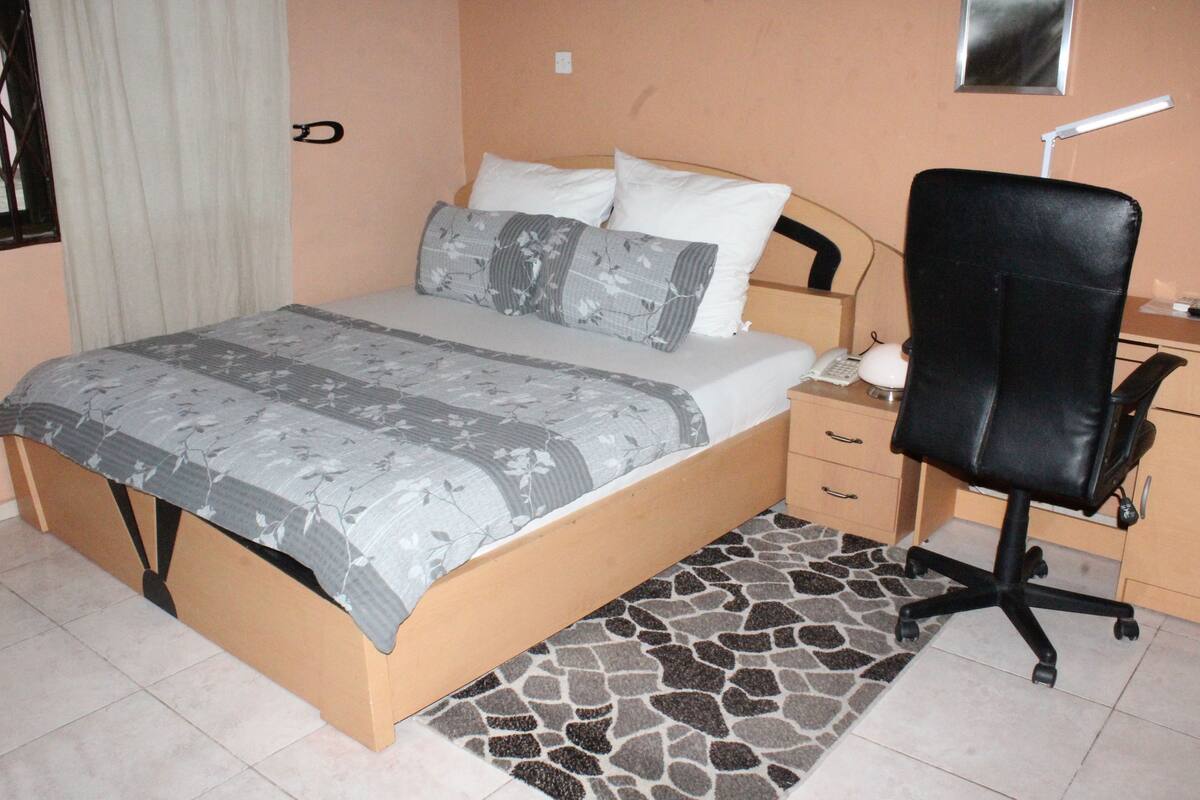 Un dormitorio con una cama, un escritorio, una silla y una alfombra pequeña.