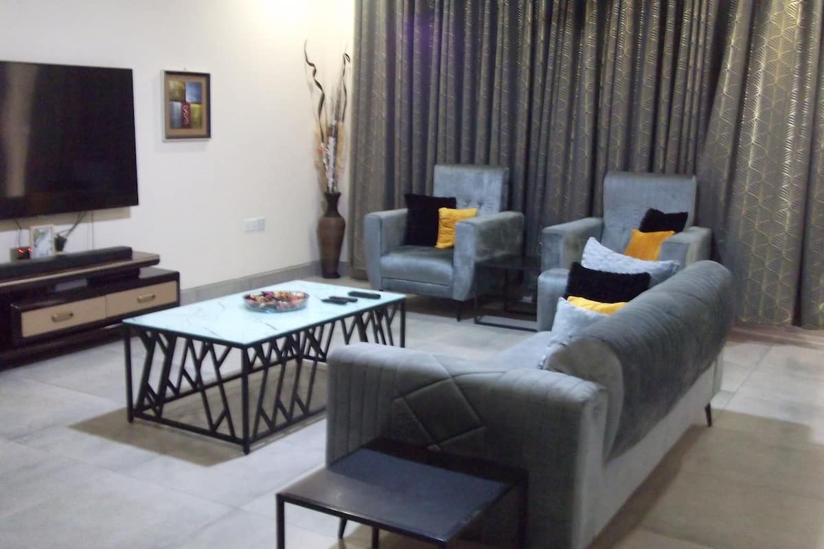 Una sala de estar con una televisión de pantalla plana, dos sillones, un sofá y una mesa de centro.