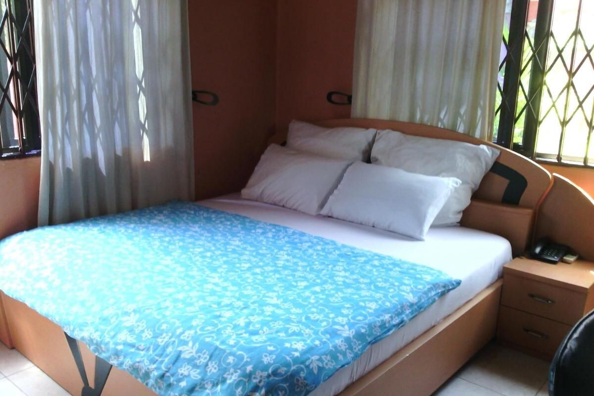 Una cama individual con colcha azul estampada, una mesita de noche con teléfono y una ventana con reja de metal.