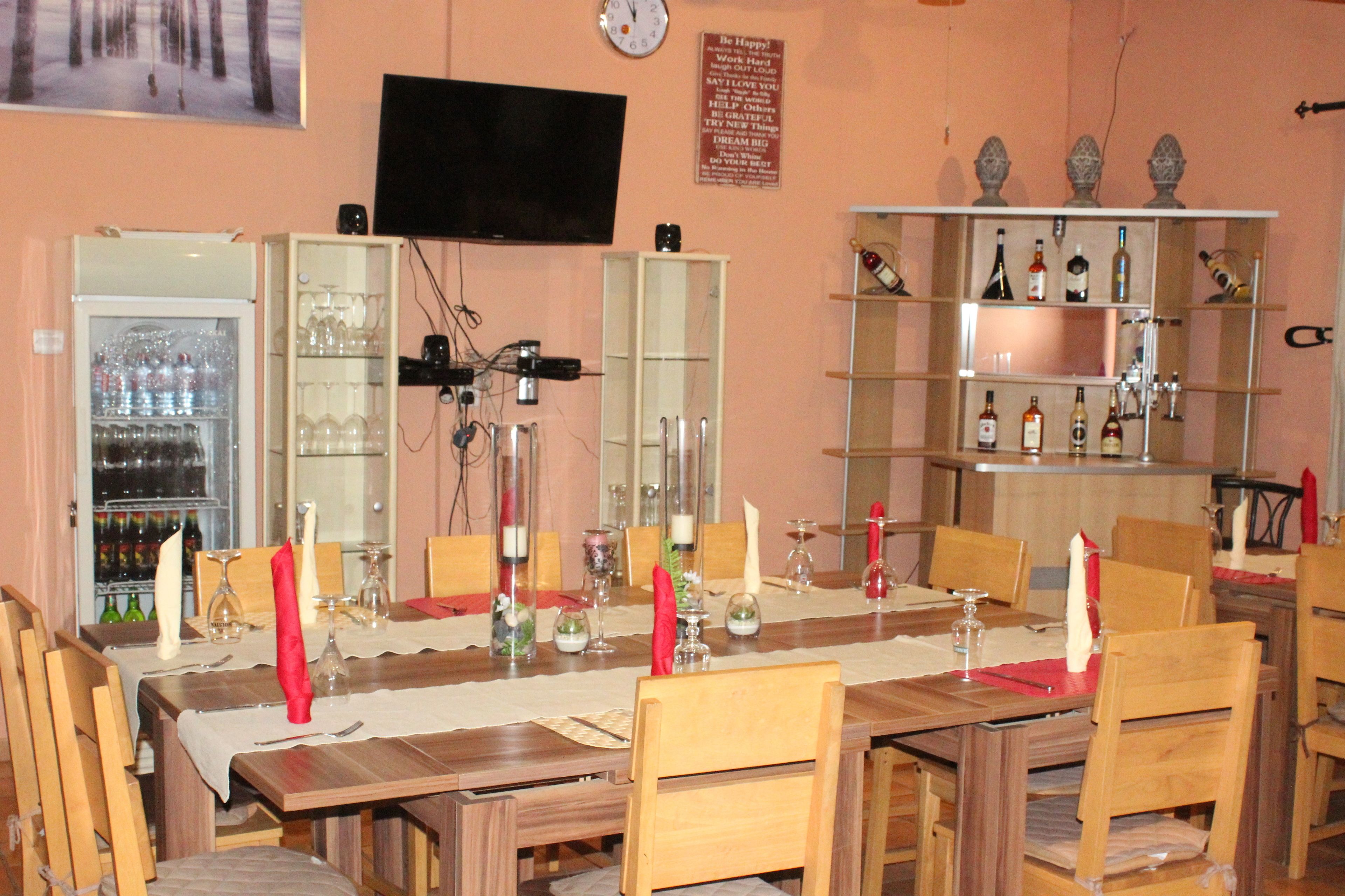 A dining area with a long wooden table set for a meal, surrounded by wooden chairs. There is a wine refrigerator and a glass cabinet with bottles.