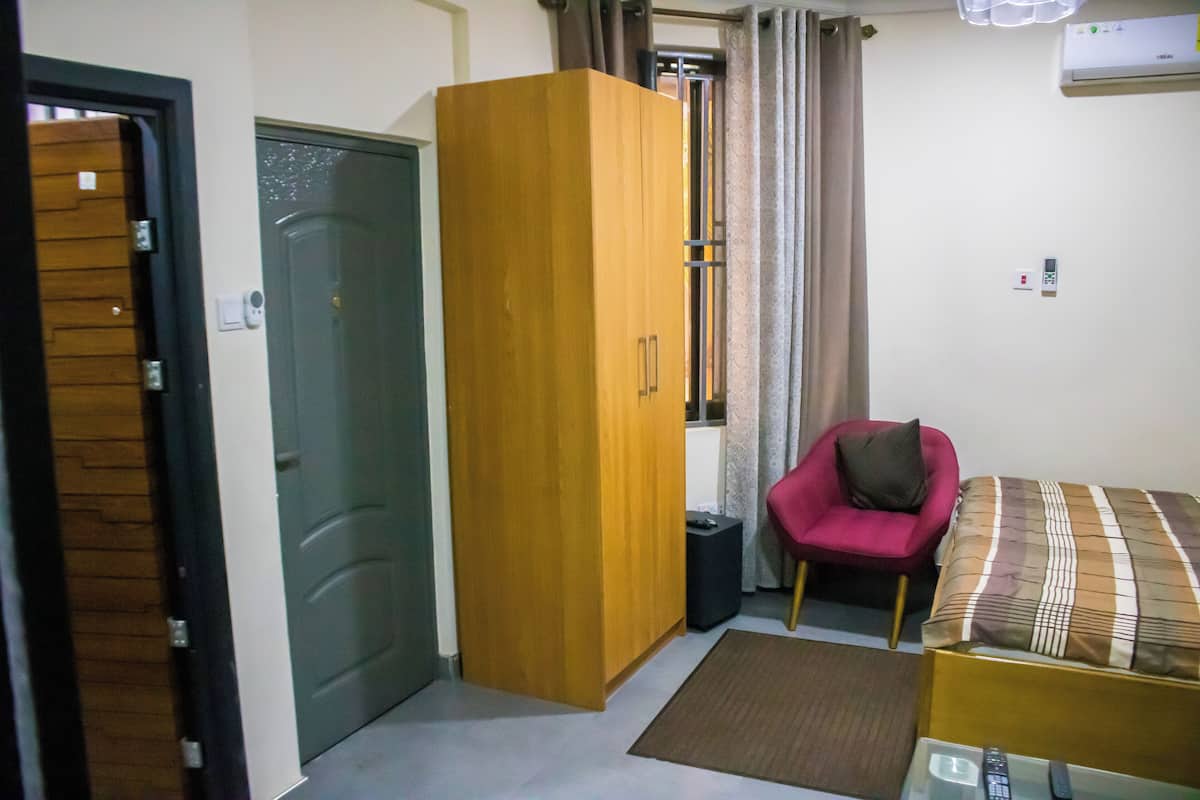 Una habitación pequeña con armario, cama, silla y una mesita.