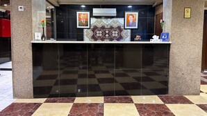 Uma área de recepção com piso xadrez, um balcão de recepção de mármore e retratos emoldurados acima.