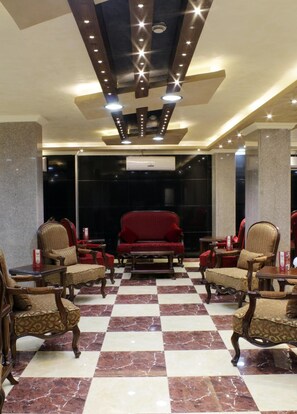 A lobby with a checkered floor, red upholstered chairs, and a central red sofa. - Alnahas Plaza Hotel (Irbid)