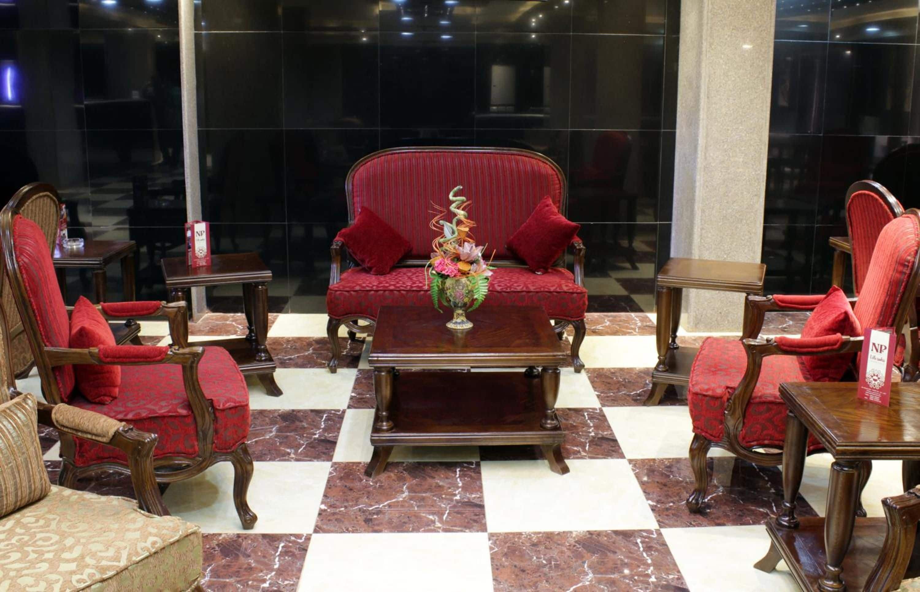 A hotel lobby with a checkered floor, a central red sofa, and matching armchairs.