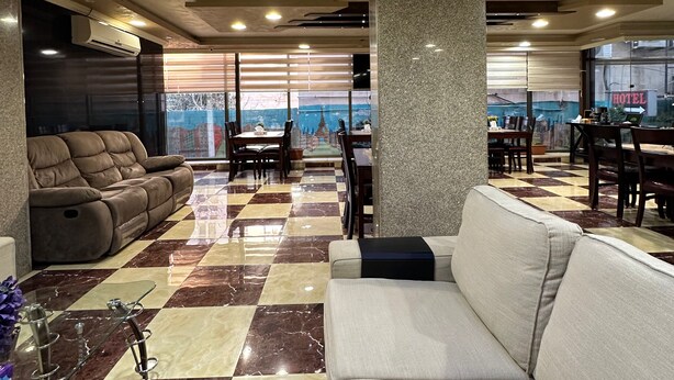 Um hall de hotel com piso xadrez, sofás, mesas de jantar e um grande pilar.