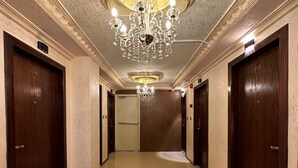 Um corredor com um candelabro, portas de madeira e um tapete estampado.