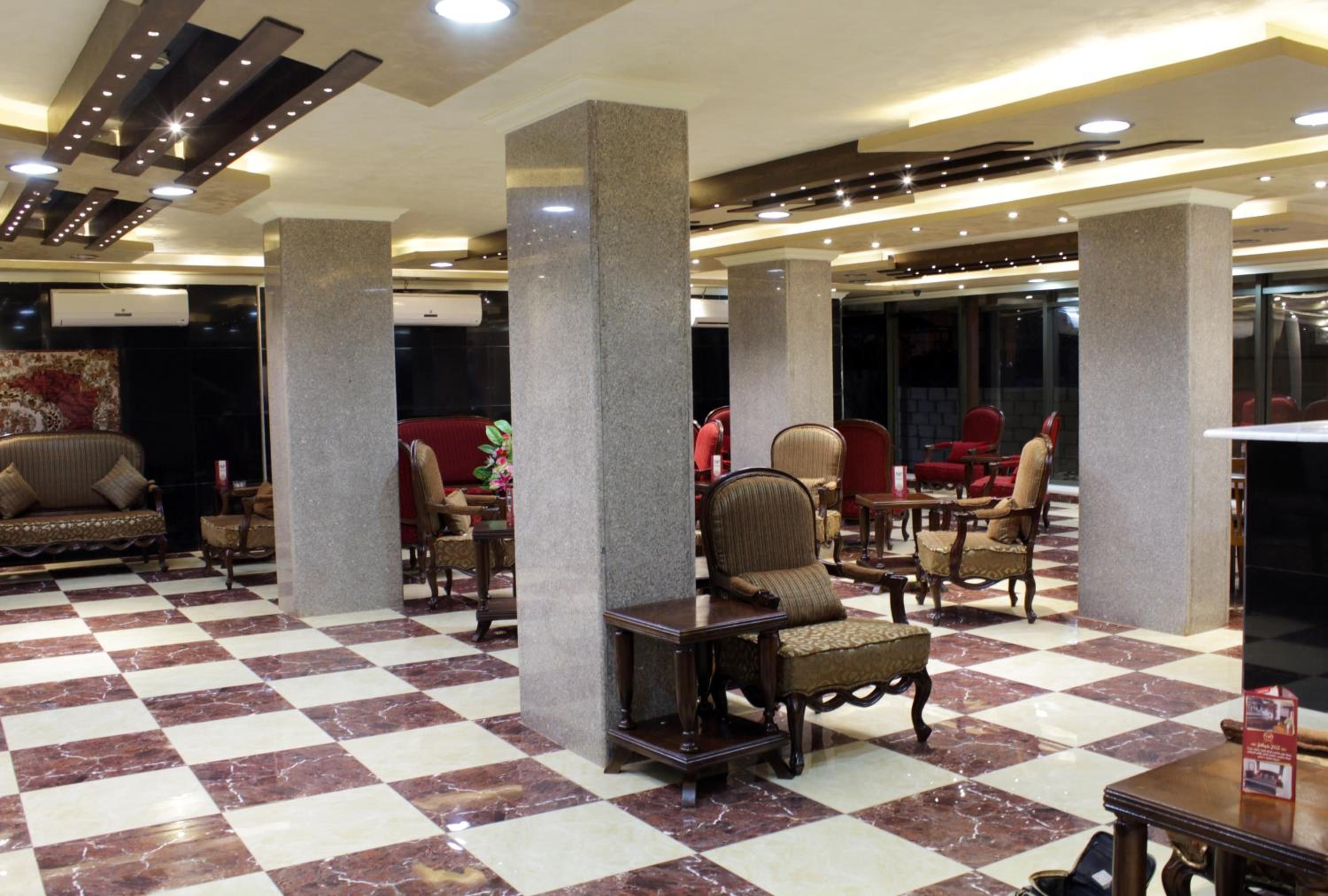 Um saguão com piso xadrez, várias áreas de estar com cadeiras e sofás, e um design de teto moderno com iluminação embutida.