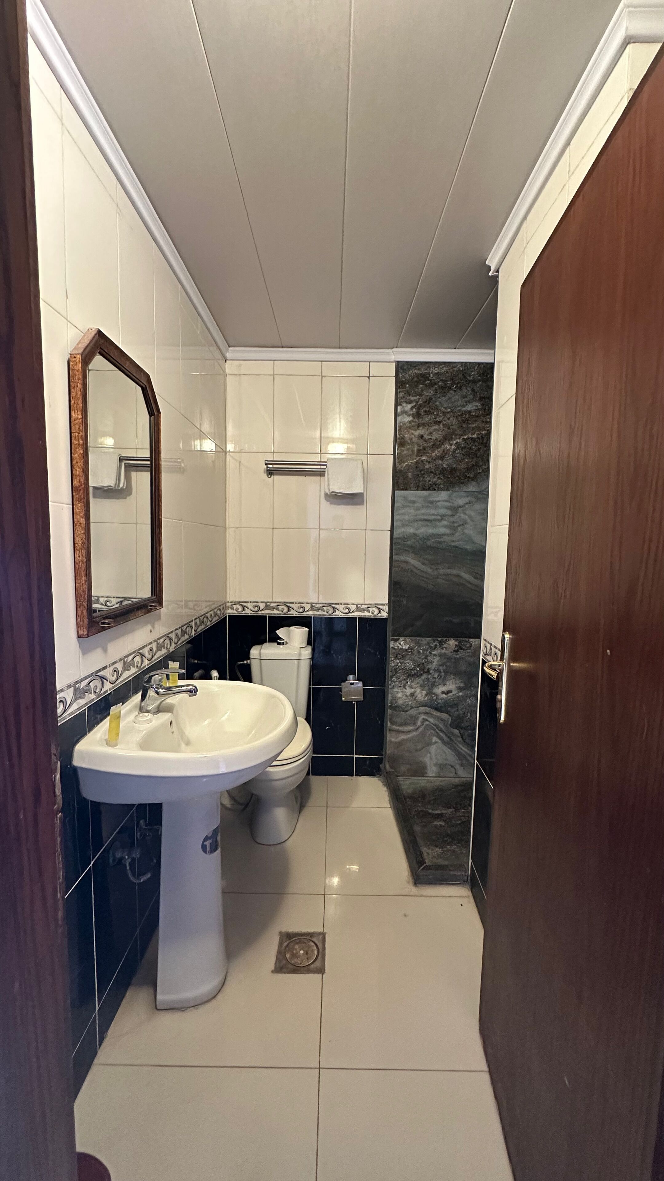 A bathroom with a white sink, toilet, and a mirror. There is a towel hanging on the wall and a door to the right.