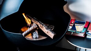 Una chimenea moderna con leños ardiendo, un libro sobre una mesita auxiliar y una pared oscura y curvada.