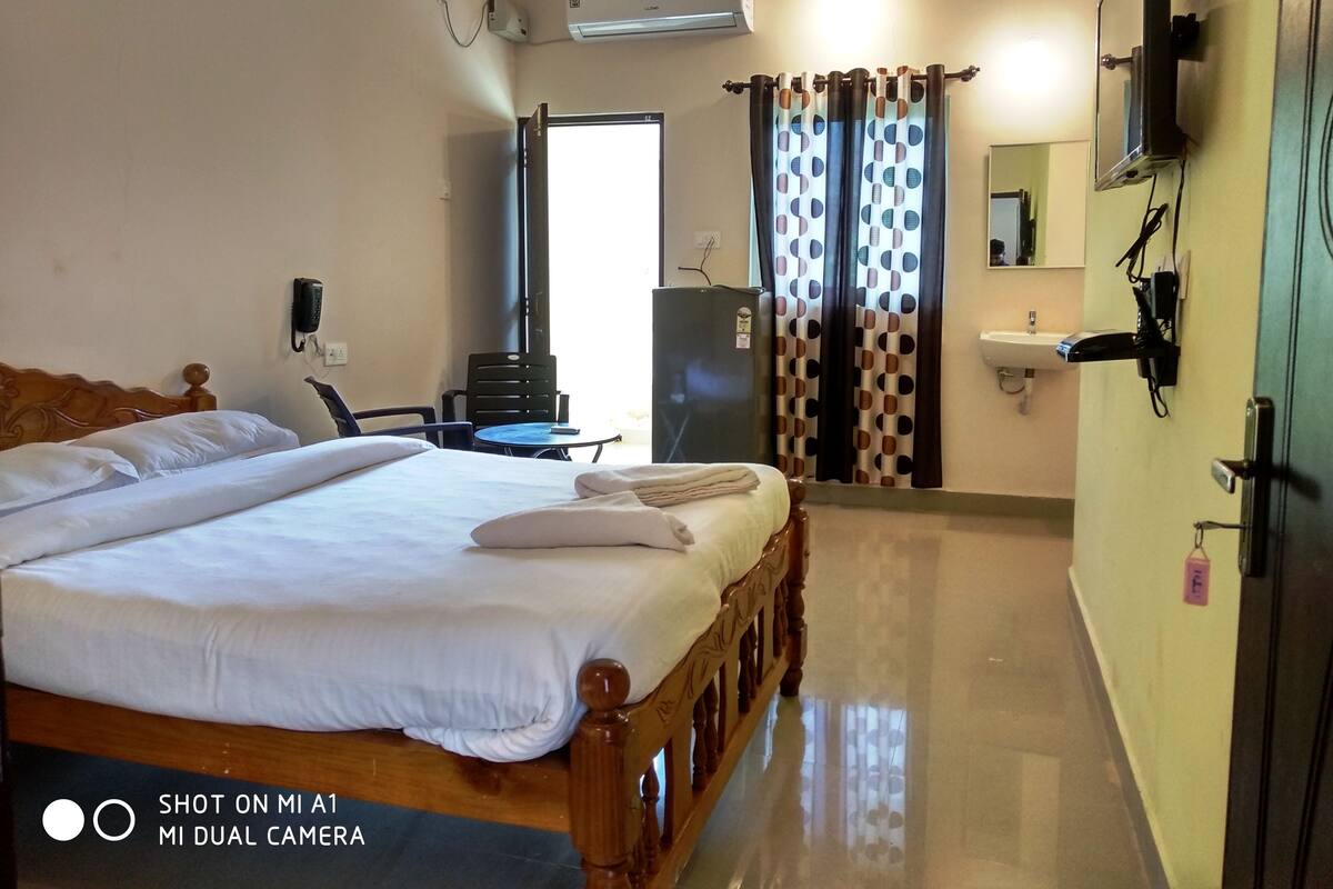 A hotel room with a bed, a desk, a chair, an air conditioner, a mirror, and a sink.