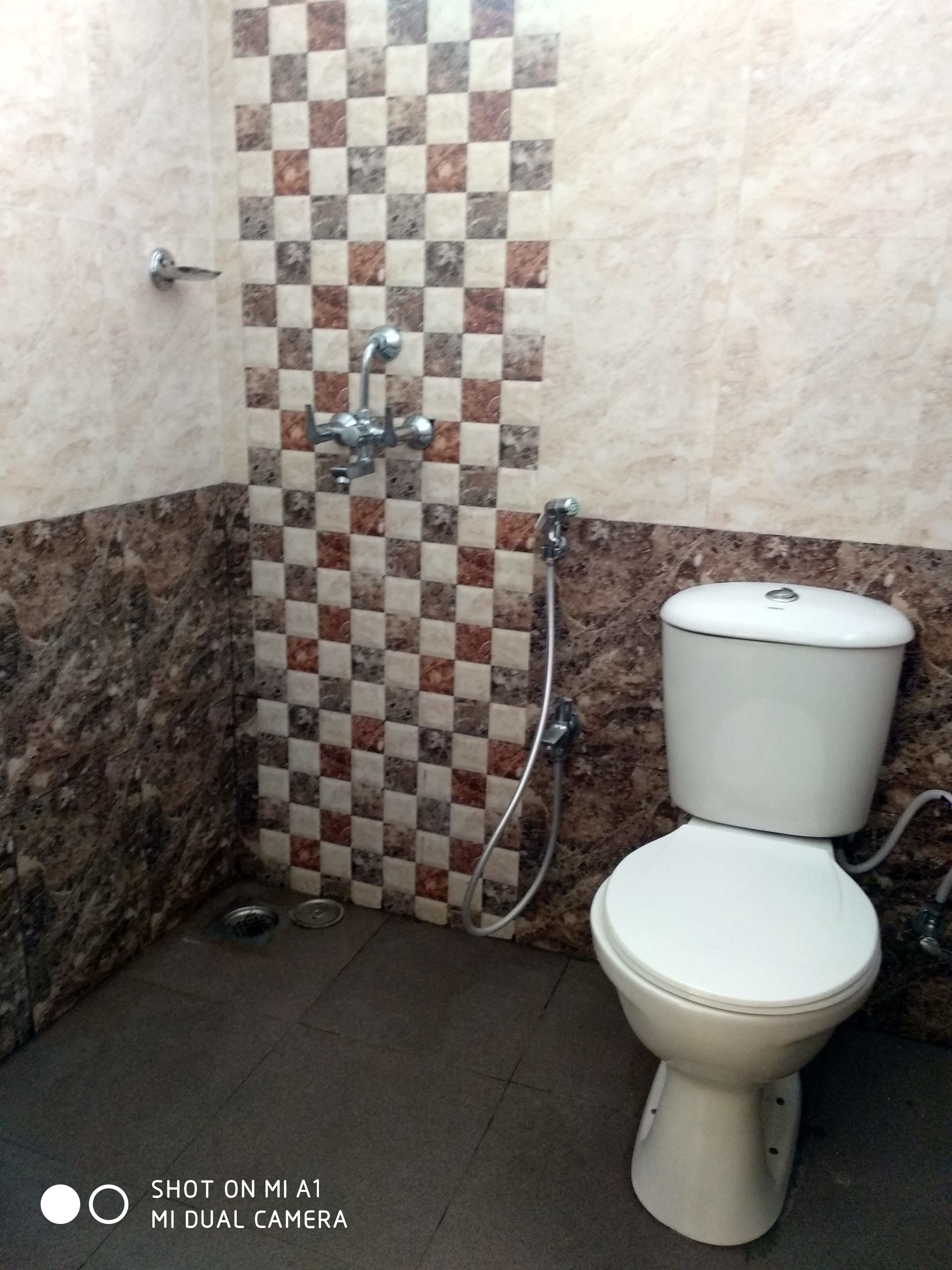 A bathroom with a tiled shower wall, a toilet, and a marble floor.